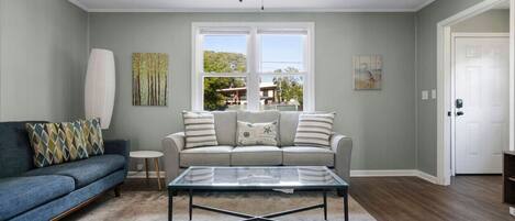 A living room with a sofa, a coffee table, a ceiling fan, and a window with a view of the outdoors.