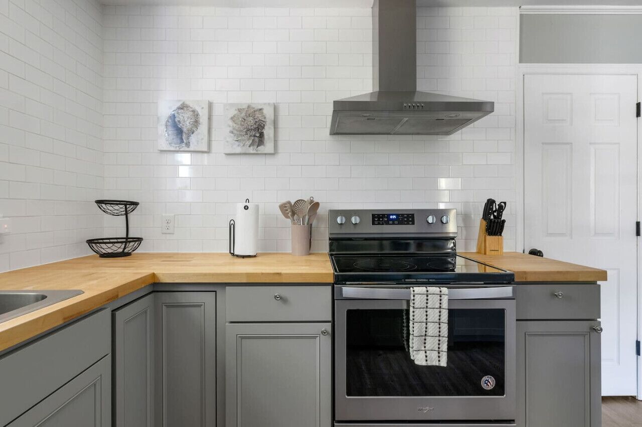 Une cuisine moderne avec des carreaux de céramique blancs disposés en motif métro, une hotte en acier inoxydable, un four encastré et un plan de travail en bois.