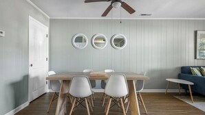 Un coin repas avec une table en bois et quatre chaises, un ventilateur de plafond et trois miroirs fixés au mur.