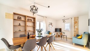 Ein modernes Wohnzimmer mit Essbereich, mit einem Holztisch, grauen Stühlen, einem blauen Sofa und einer Wand mit Steinverkleidung.