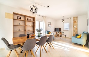 Een moderne woonkamer met een eethoek, met een houten eettafel, grijze stoelen, een blauwe bank en een accentmuur van steen.
