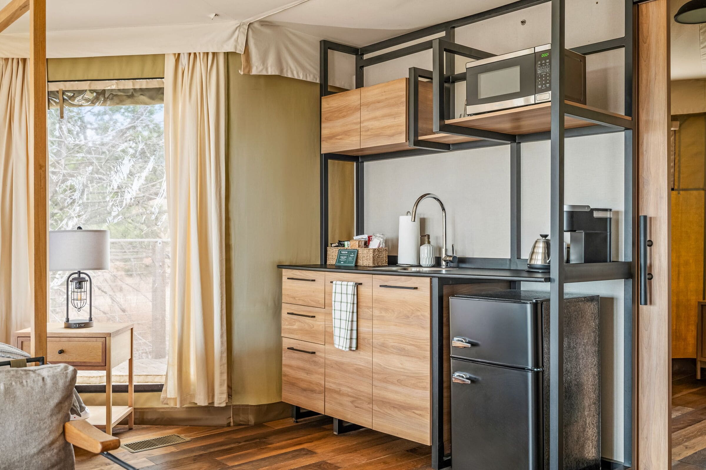 Una cocina compacta con armarios de madera, un refrigerador negro y un microondas.