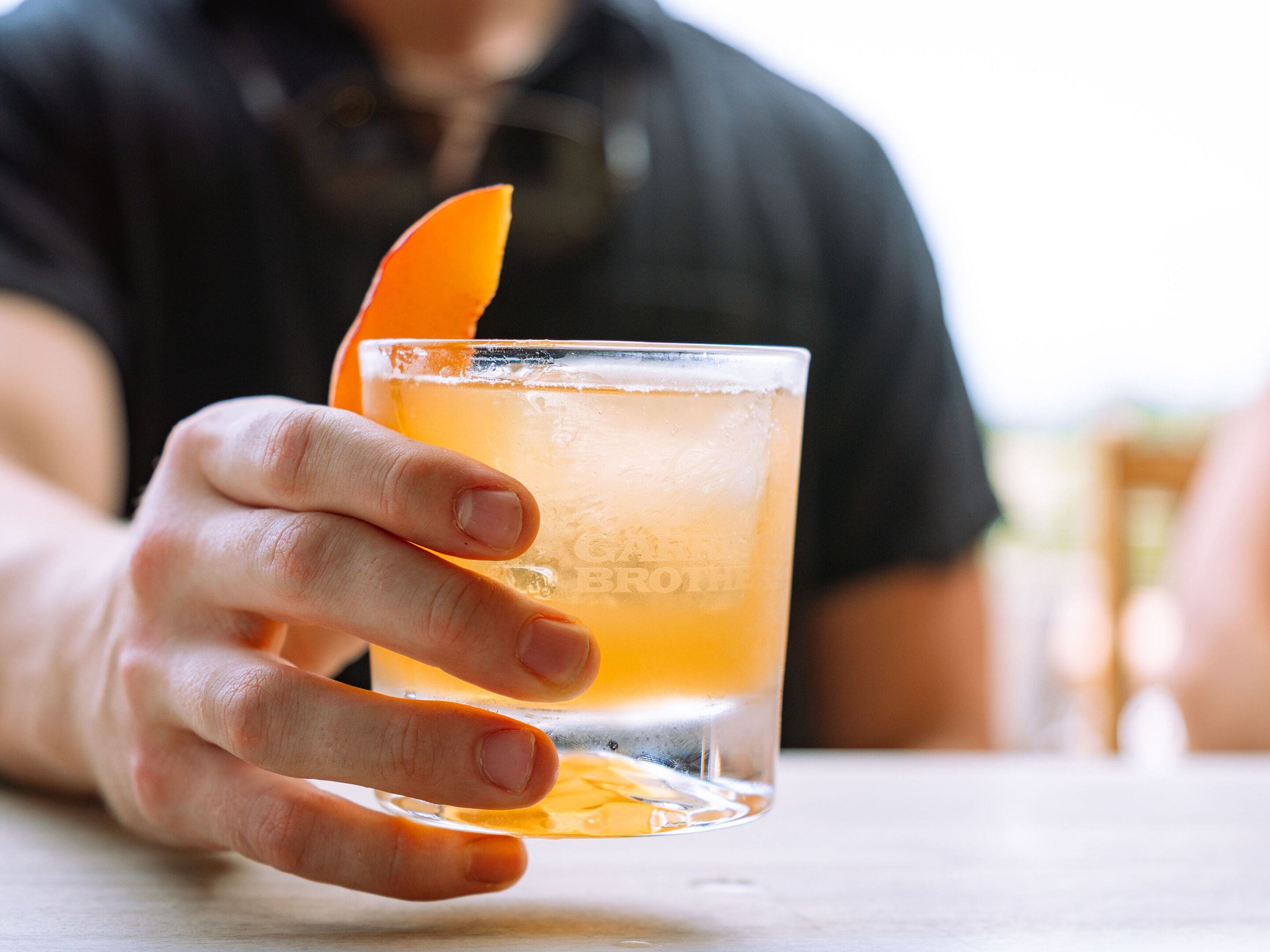 Eine Hand hält ein Glas mit einer klaren Flüssigkeit und einer Orangenscheibe.