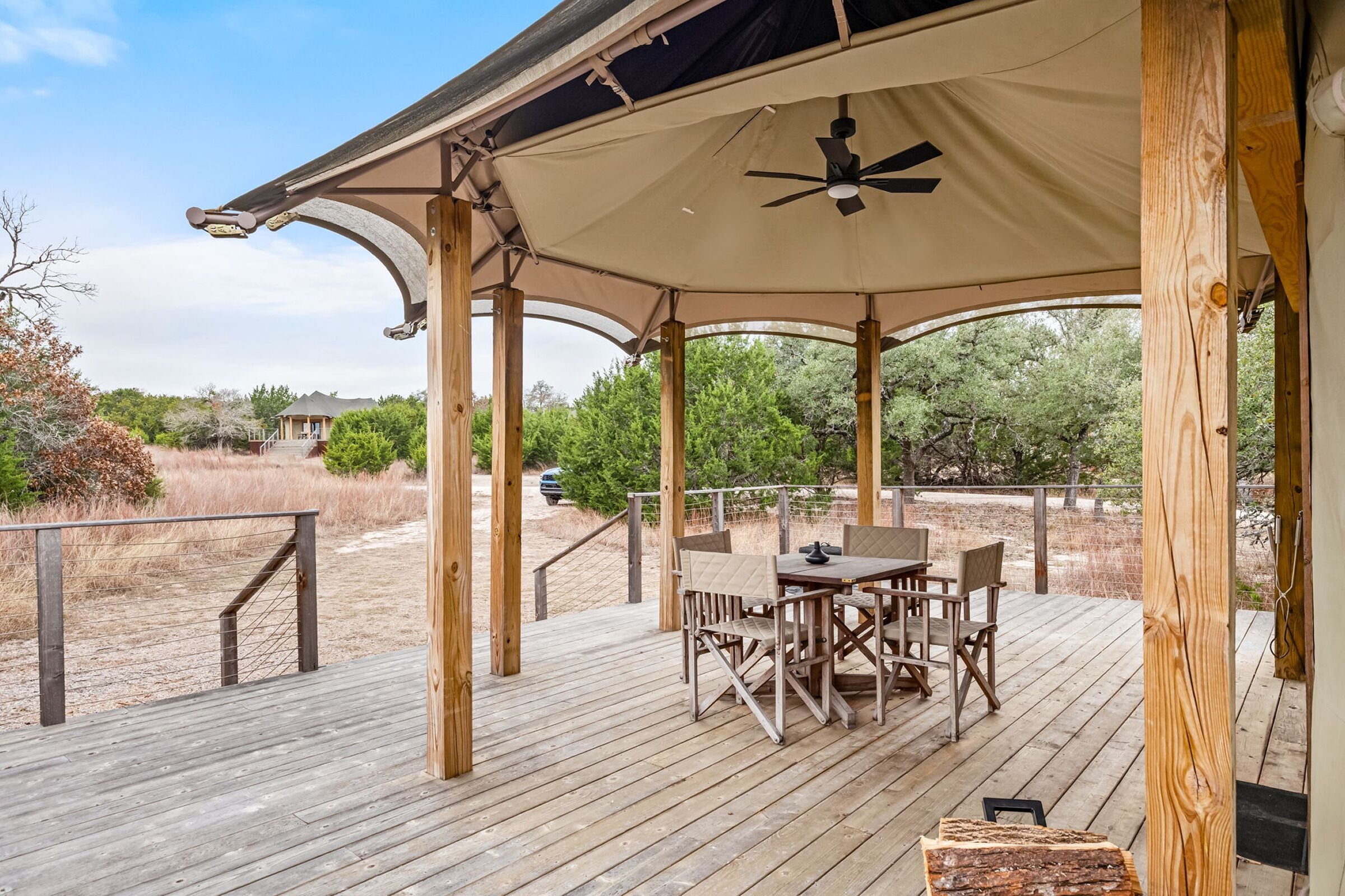 A covered outdoor patio with a table and chairs, a ceiling fan, and a view of the surrounding landscape.