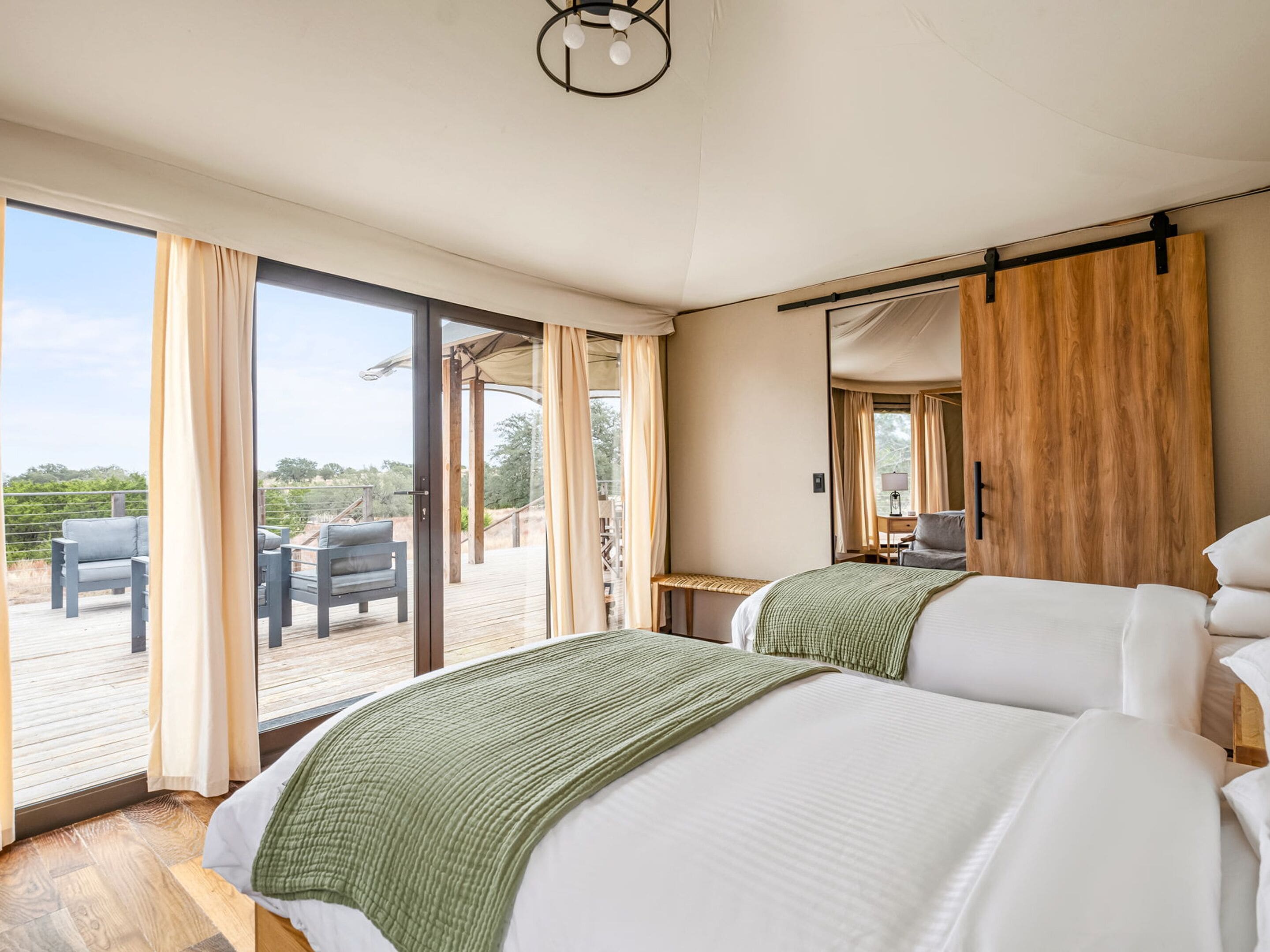Habitación de hotel con dos camas, un armario de madera, un escritorio con lámpara y un balcón con mobiliario exterior.