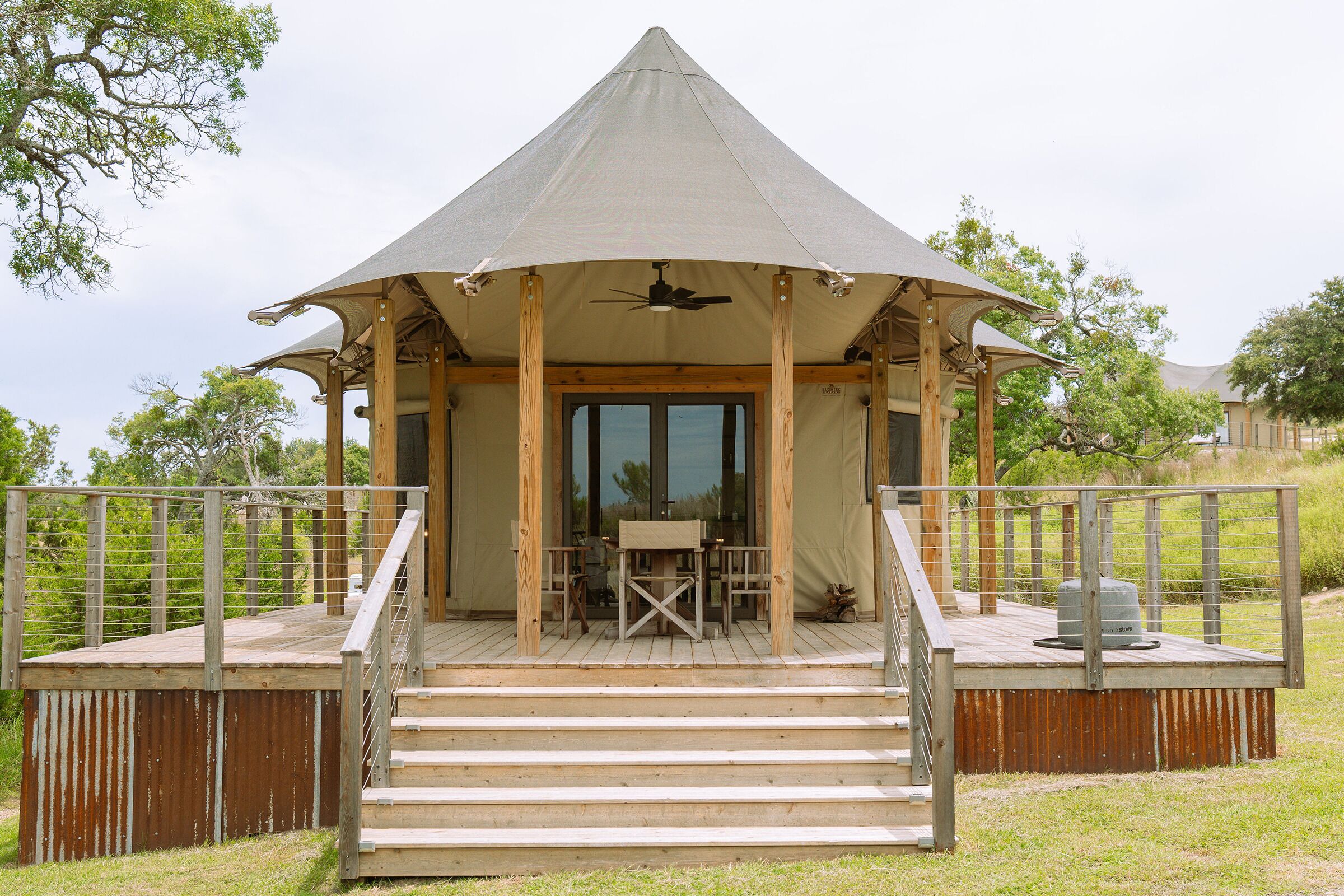 A wooden deck with a covered seating area, a ceiling fan, and a view of the surrounding landscape.
