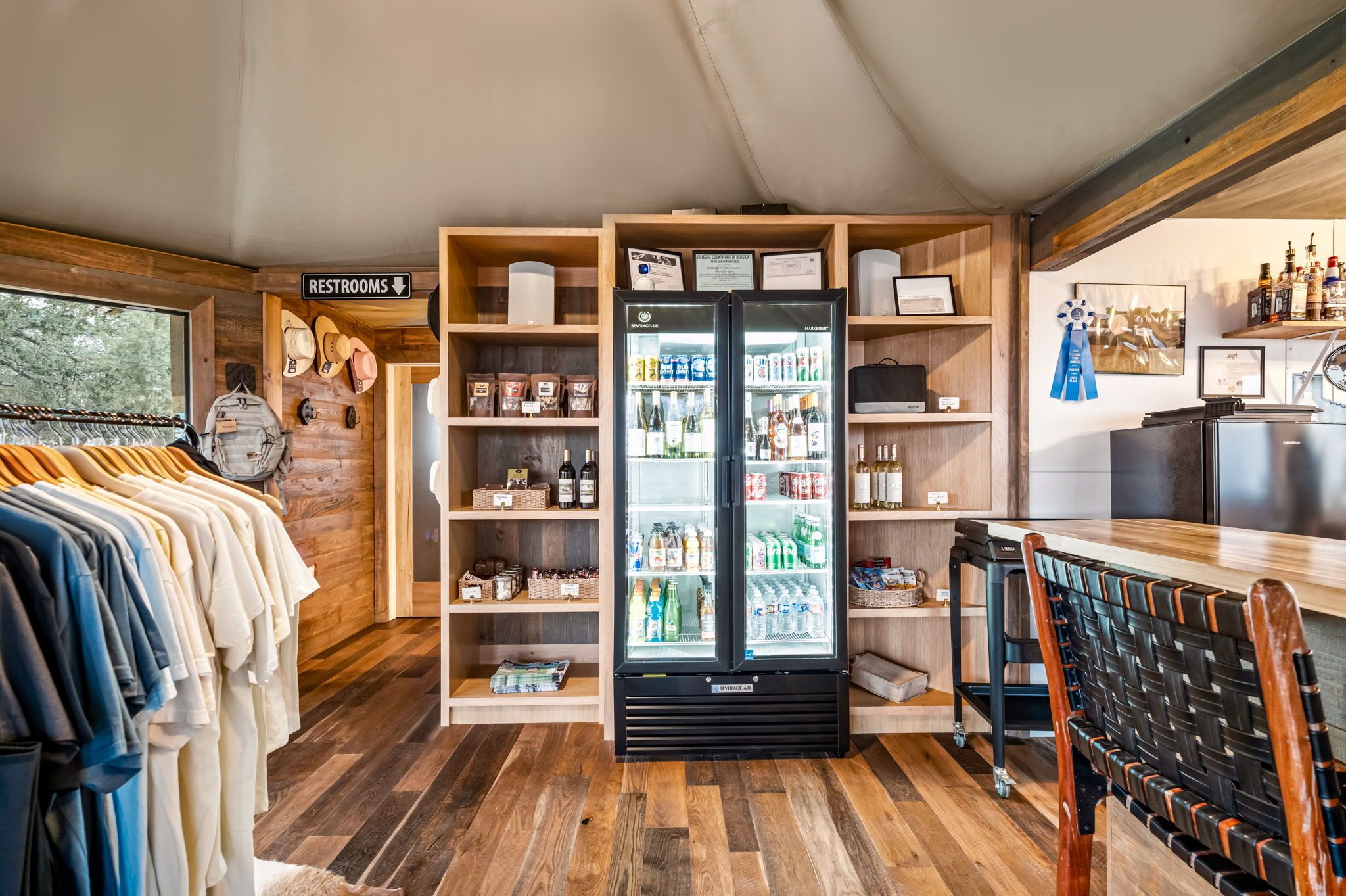 A room with a clothing rack, a refrigerator stocked with beverages, and a sign indicating restrooms.