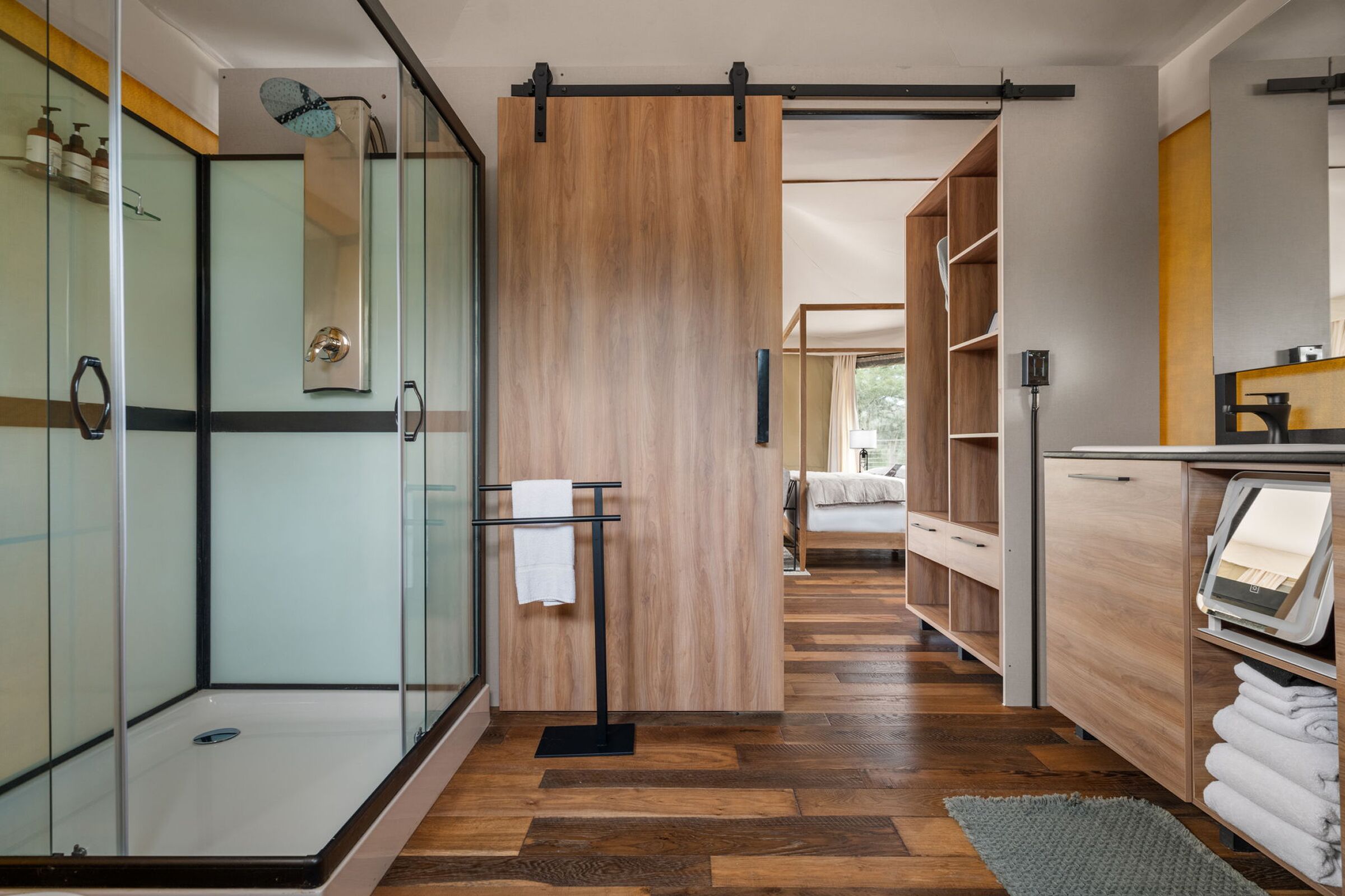 A modern bathroom with a glass shower enclosure, wooden sliding doors, a built-in toilet, and a visible towel rack.