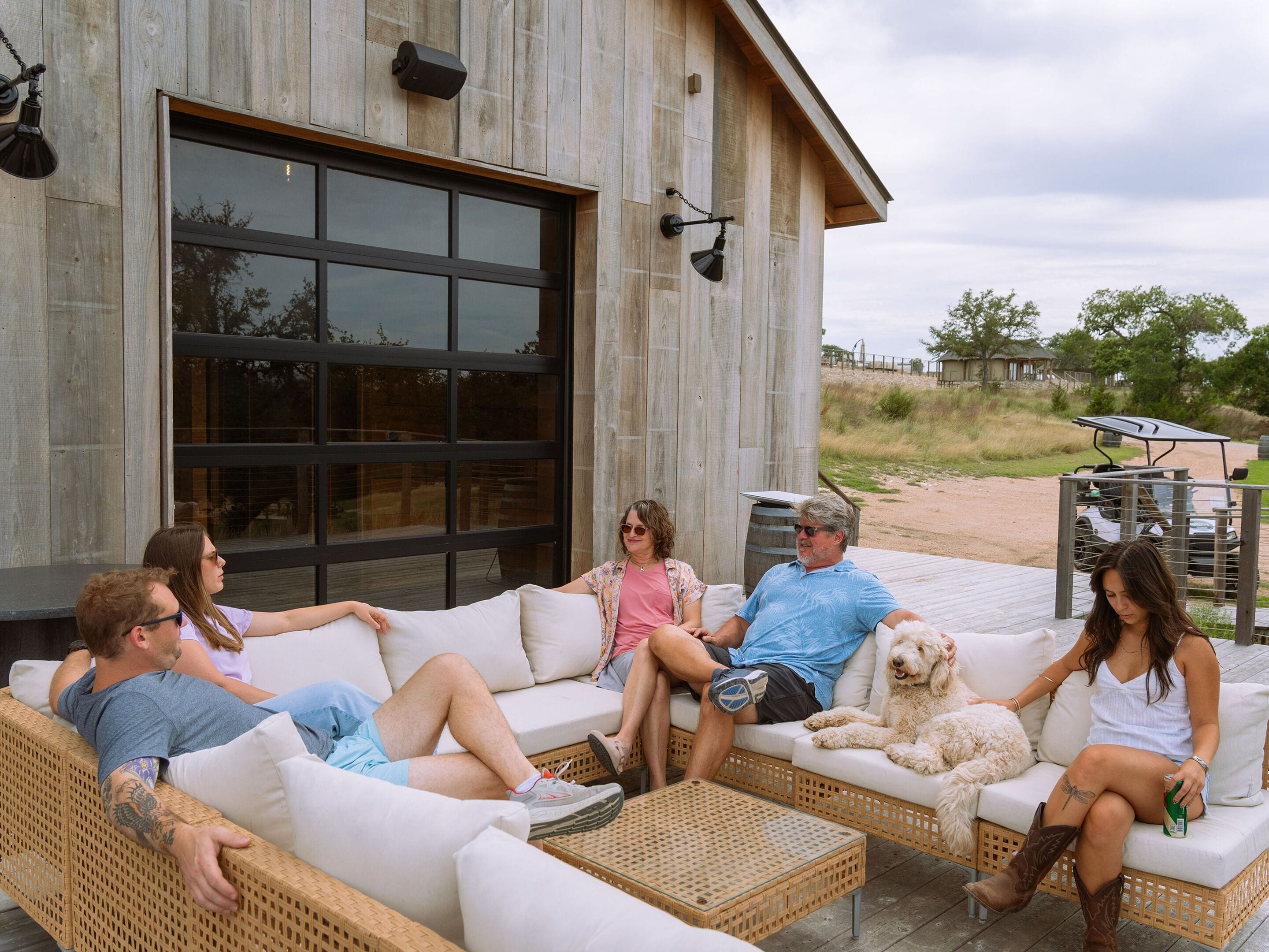 A group of people relaxing on outdoor wicker furniture in front of a building with a large garage door.