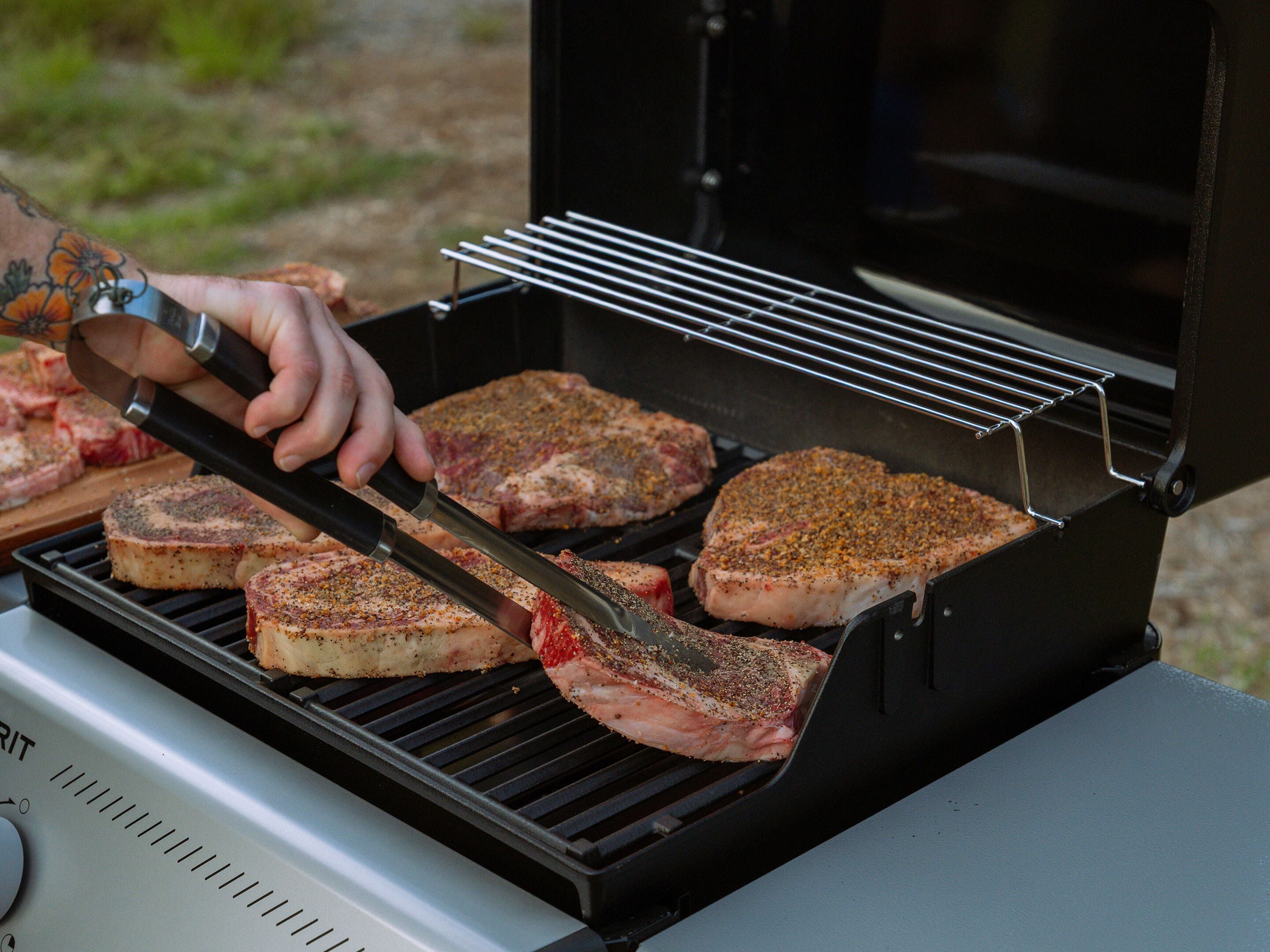 A person grilling steaks on an outdoor grill.