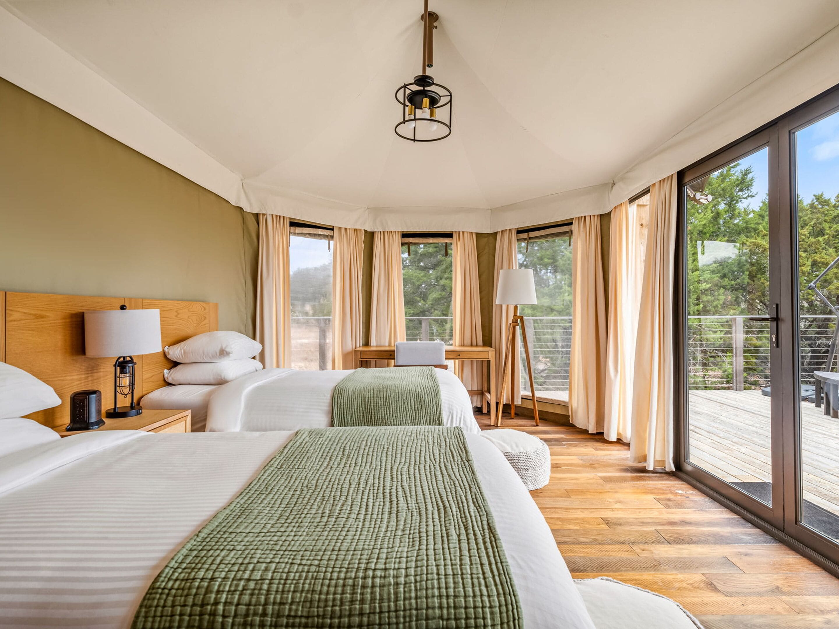 A hotel room with a large bed, a desk, a chair, and a balcony with a view of trees.