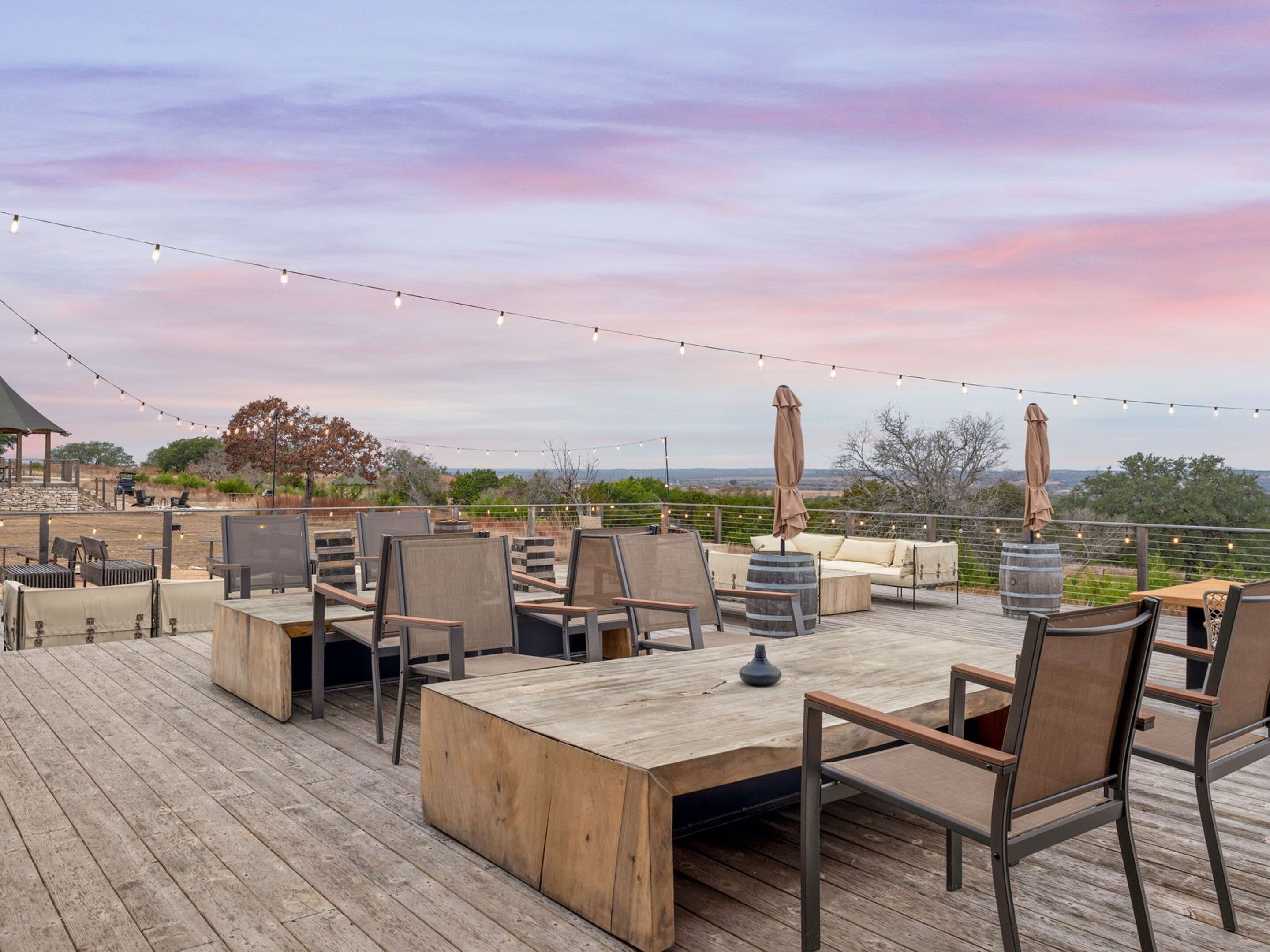 An outdoor deck with wooden furniture, string lights, and a view of the landscape.