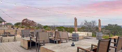 Una terraza al aire libre con mobiliario de madera, luces colgantes y vistas del paisaje.