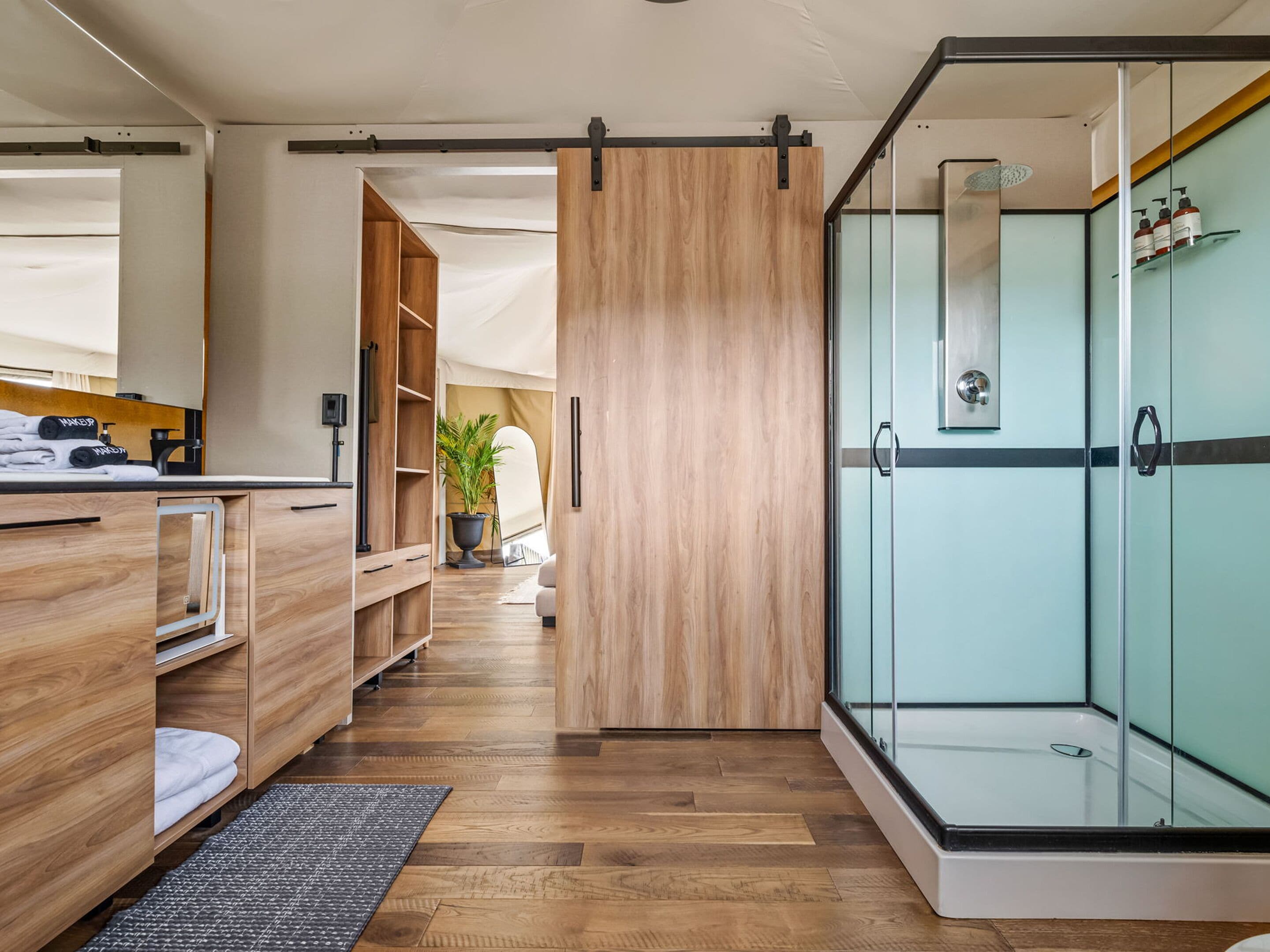 A modern bathroom with a wooden vanity, a glass shower enclosure, and a potted plant.