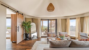 Een ruime woonkamer met een bank, een eettafel en een groot raam met uitzicht op de omgeving.