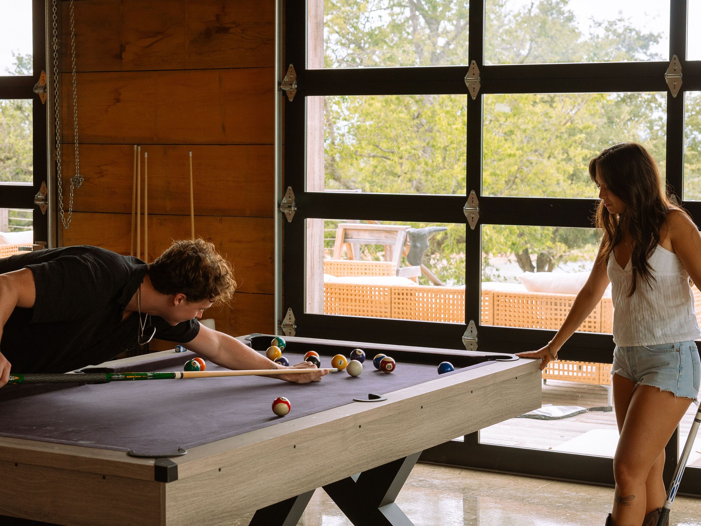 A pool table with balls, a person playing, and another observing.