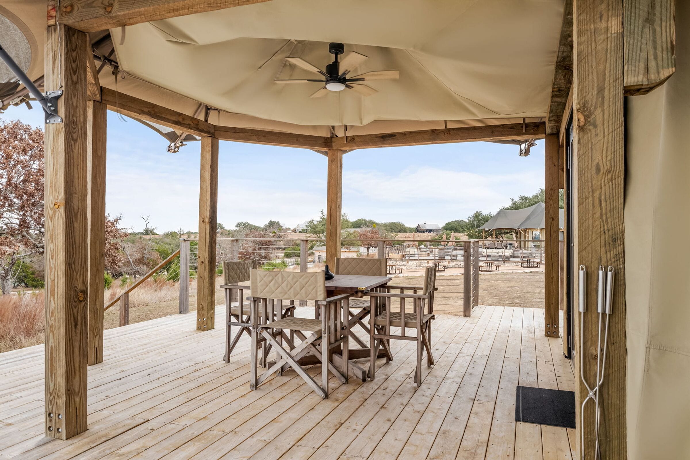 A covered outdoor seating area with a table and chairs, wooden deck, and a view of the surrounding landscape.