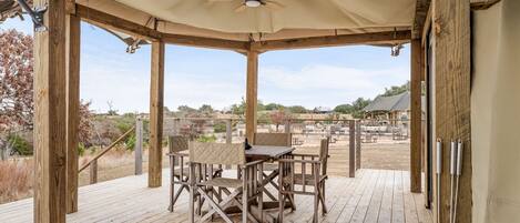 A covered outdoor seating area with a table and chairs, wooden deck, and a view of the surrounding landscape.