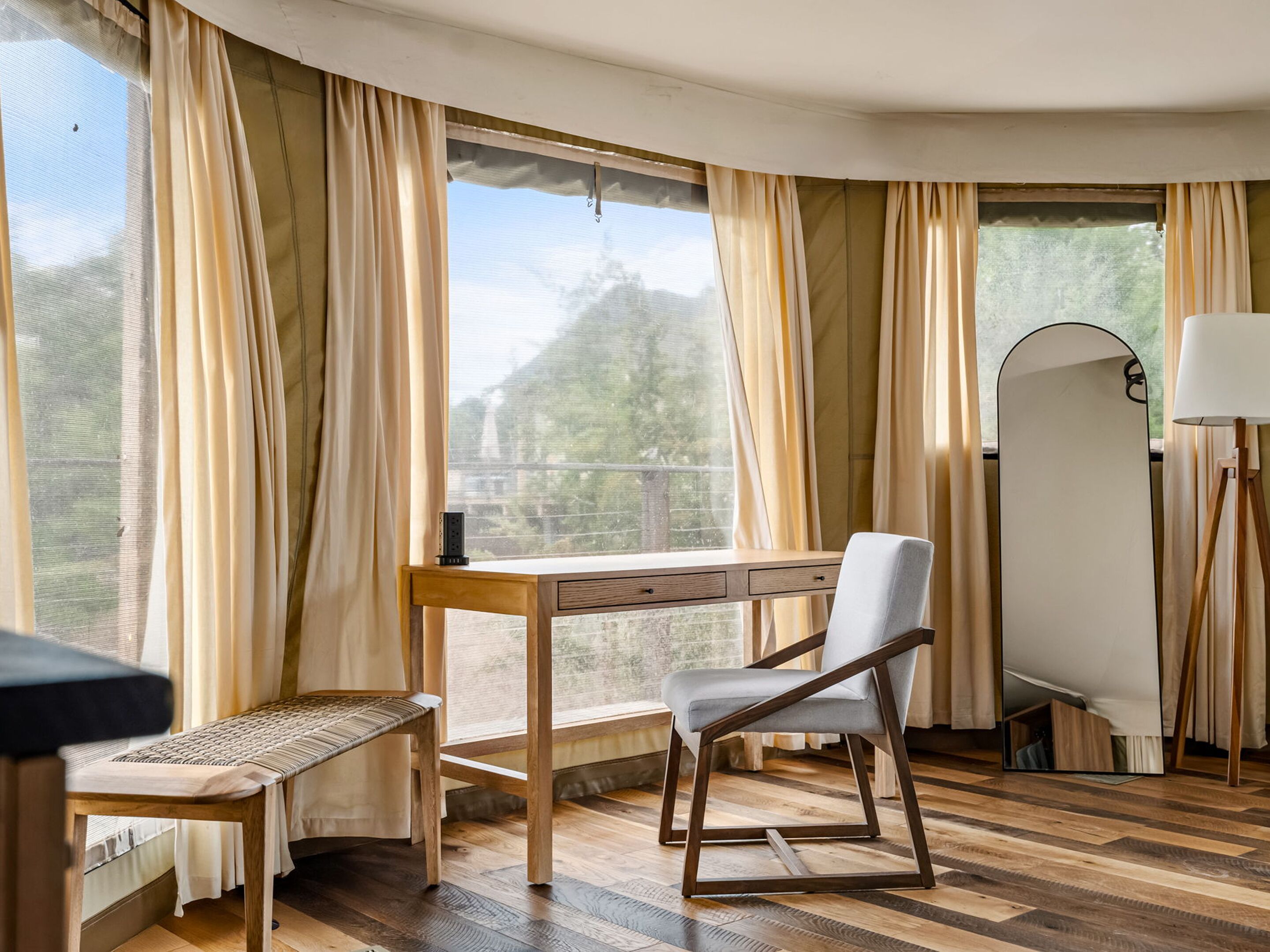 Una habitación con un escritorio de madera, una silla, un banco y un espejo grande.