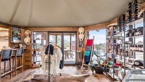 Een rustiek interieur met houten wanden, een vachttapijt, een kledingrek en planken vol hoeden en andere spullen.