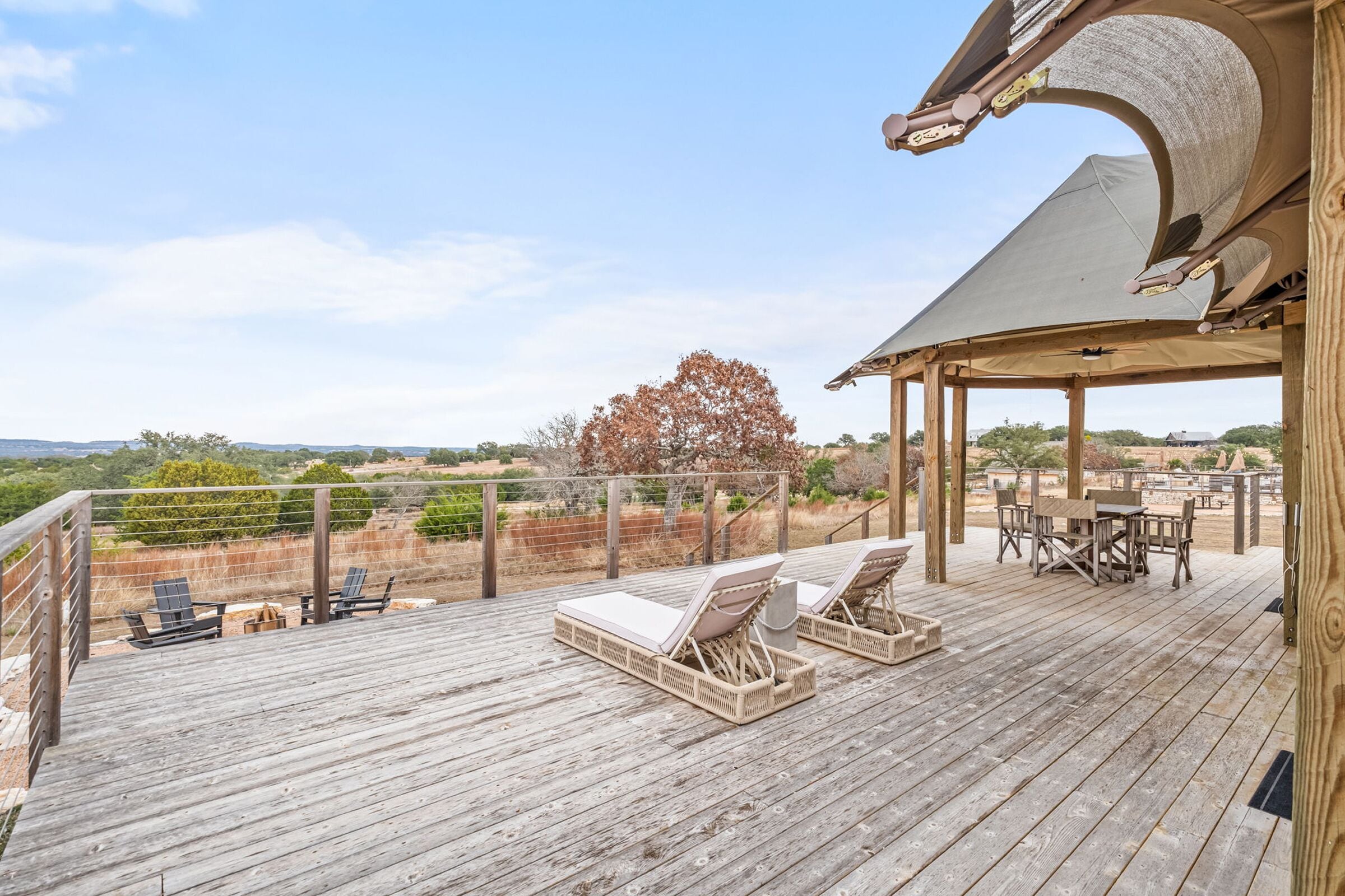 Terraza de madera con sillones de descanso y una mesa, con vistas a un paisaje pintoresco.