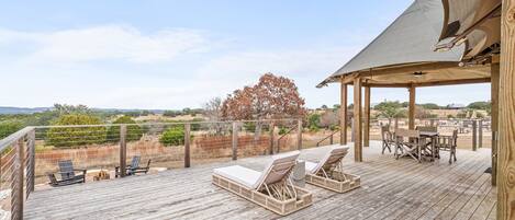 Terraza de madera con sillones de descanso y una mesa, con vistas a un paisaje pintoresco.