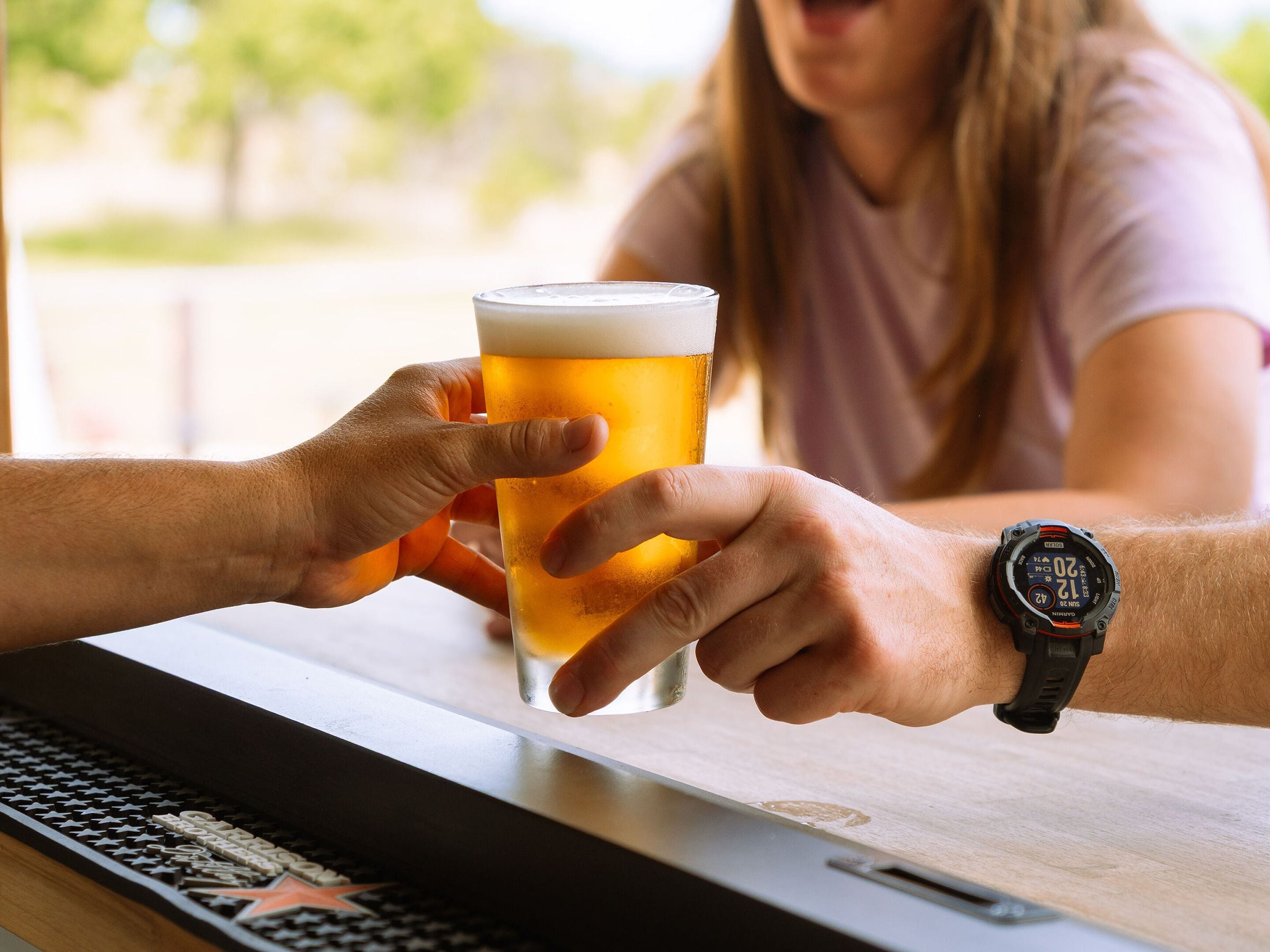 A person holding a beer glass at a bar with a watch on their wrist.