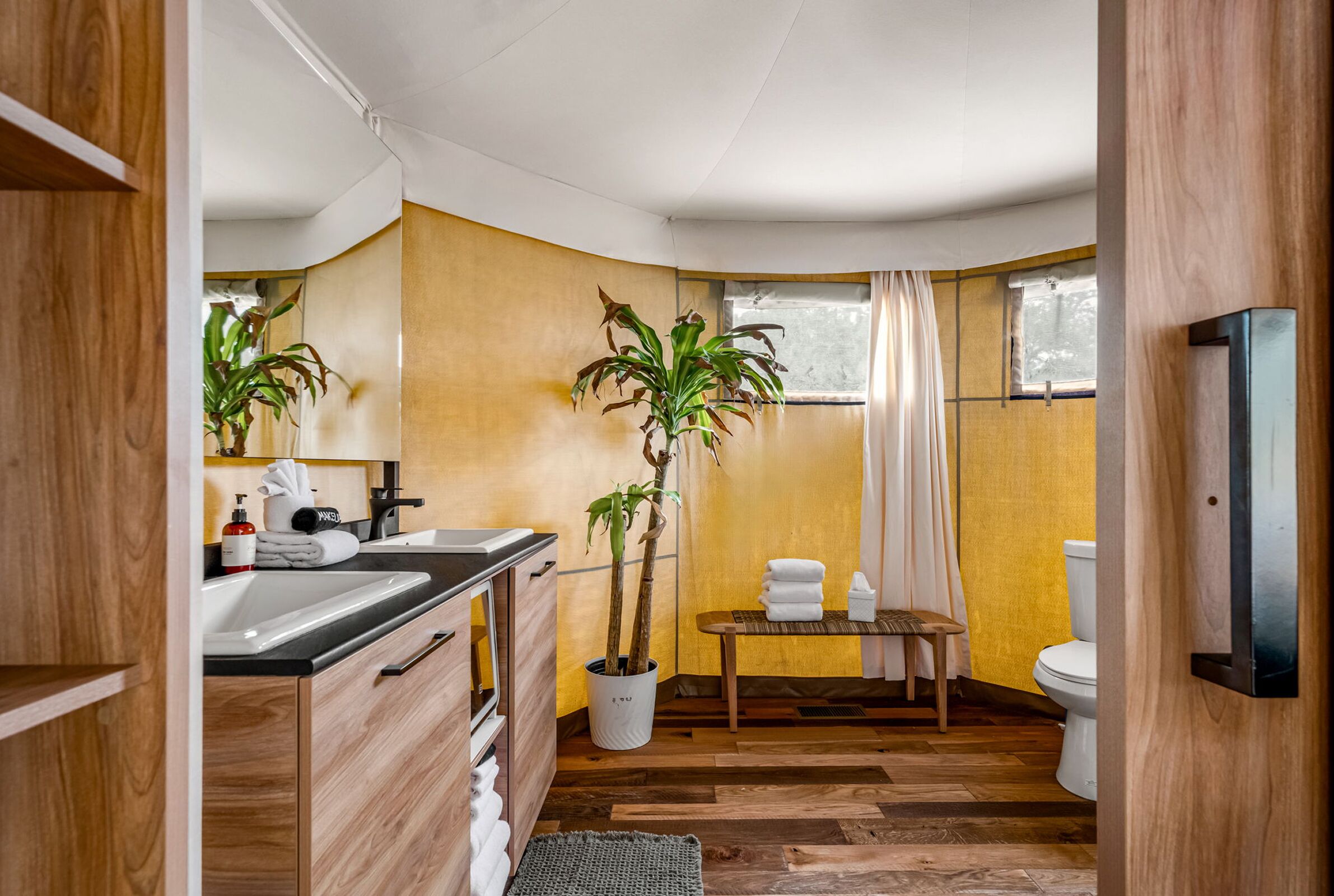 A modern bathroom with wooden flooring, a sink, a toilet, and a small table with towels.