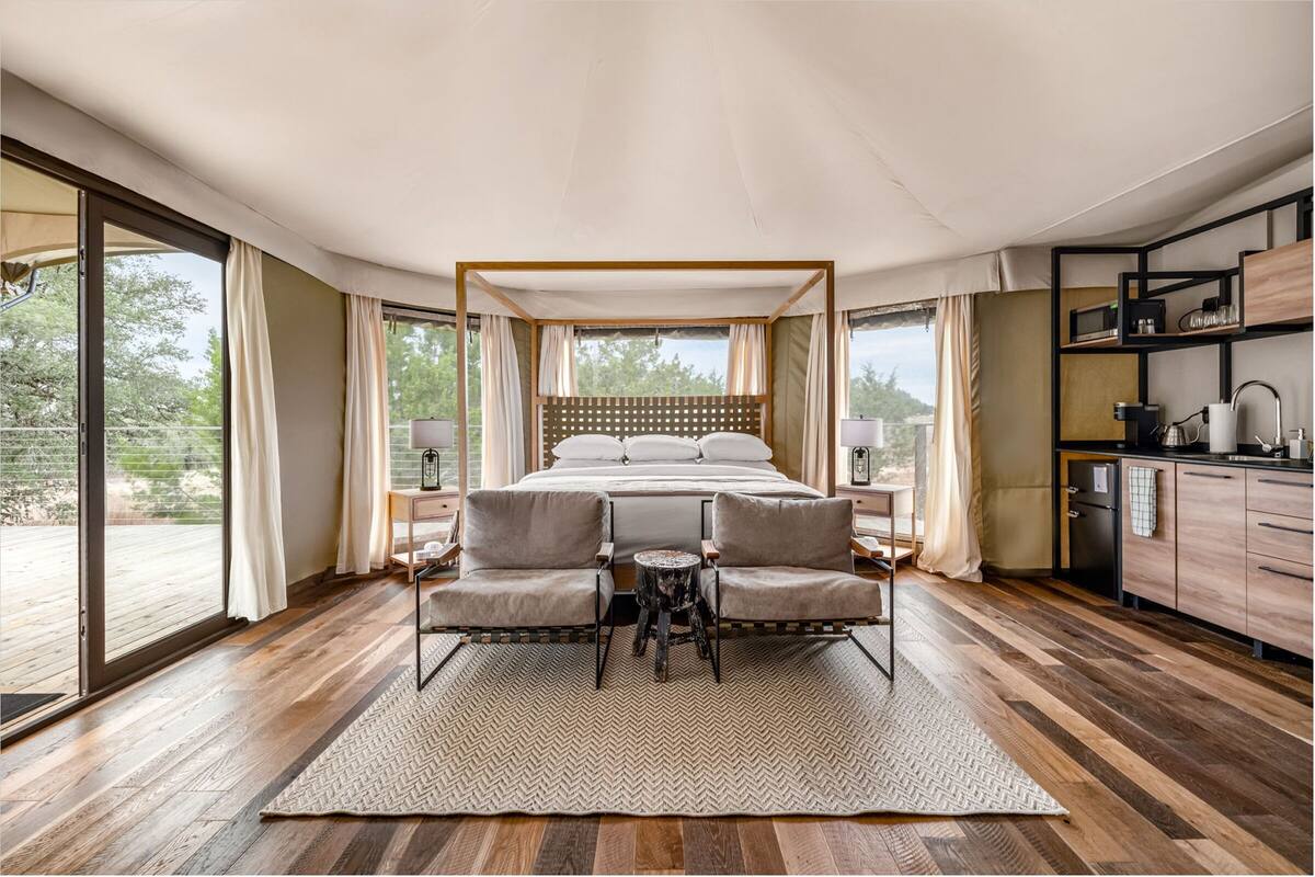 Une chambre à coucher avec un lit à baldaquin, une petite table, deux chaises et une vue sur l’extérieur.