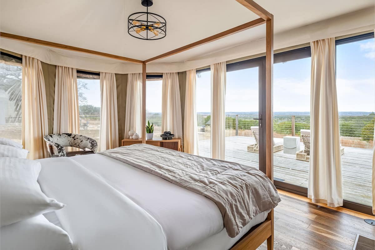 Une chambre dotée d’un grand lit, d’un plafond en bois et offrant une vue sur l’extérieur grâce à de grandes fenêtres.
