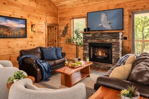 Ein gemütliches Blockhaus-Interieur mit Kamin, Ledersofas und einem darüber montierten Fernseher.