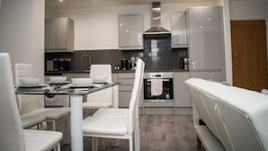 A modern kitchen with white cabinetry, a built-in oven, and a dining area with a glass table and white chairs.