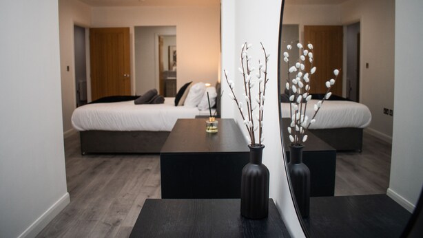 A modern hotel room with a large bed, a dark wooden coffee table, and a vase with branches.