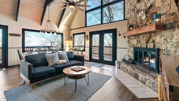 A spacious living room with a stone fireplace, large windows, and a cozy seating area. - Free Dollywood Tix/Views/Pool/Dog Friendly/Private (Gatlinburg)