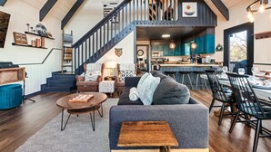 A spacious loft with a high ceiling, exposed beams, a staircase, a cozy seating area with a sofa and coffee table, and a kitchen with teal cabinets. - Free Dollywood Tix/Views/Pool/Dog Friendly/Private (Gatlinburg)