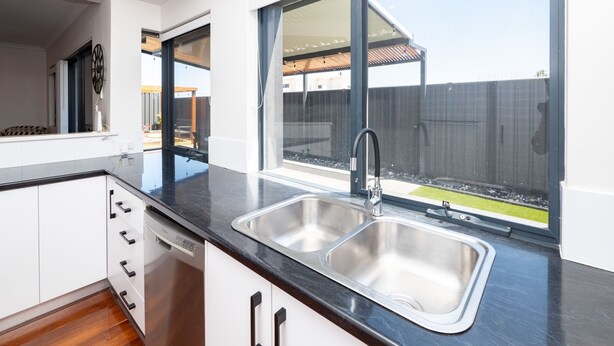 A modern kitchen with a double sink, white cabinets, and a view of the backyard through large windows.