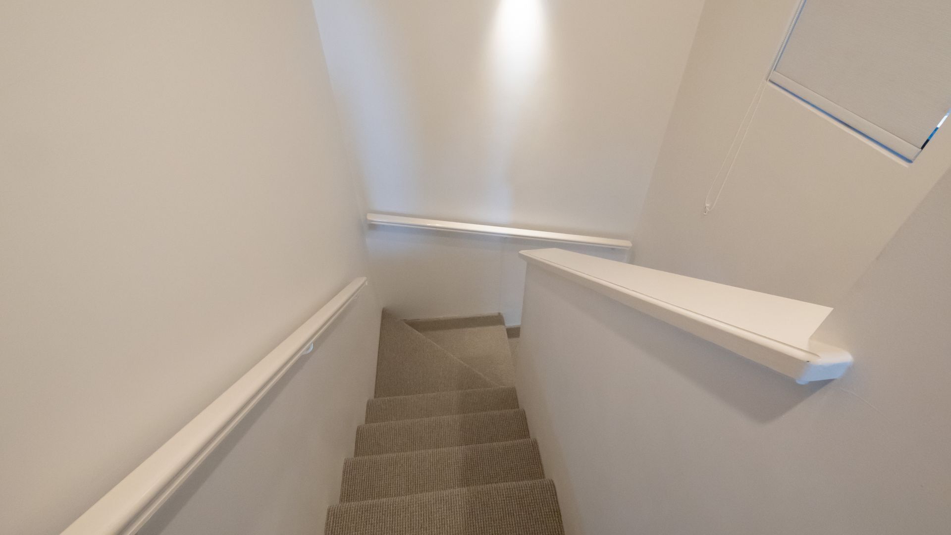 A narrow stairway with a carpeted landing and a white handrail.