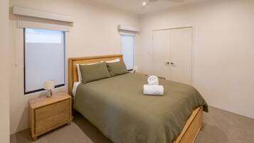 A neatly arranged bedroom with a bed, bedside tables, a wardrobe, and two windows with blinds.