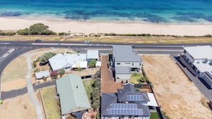 An aerial view of a coastal residential area with houses, a road, and a beach.