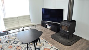 A modern living room with a sofa, a TV, a table, and a wood-burning stove. - Spacious sun filled home (South West Rocks)