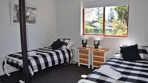 Two single beds with checkered bedding, a dresser, and lamps create a cozy retreat with a serene view.
