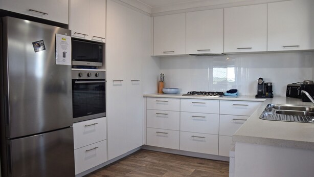 A modern kitchen with stainless steel appliances, white cabinetry, and a tiled backsplash. - Spacious sun filled home (South West Rocks)