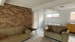 A living room with two sofas, a small table, and a brick wall. - Spacious sun filled home (South West Rocks)