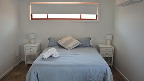 A bedroom with a bed, two bedside tables, a window, and an air conditioning unit. - Spacious sun filled home (South West Rocks)