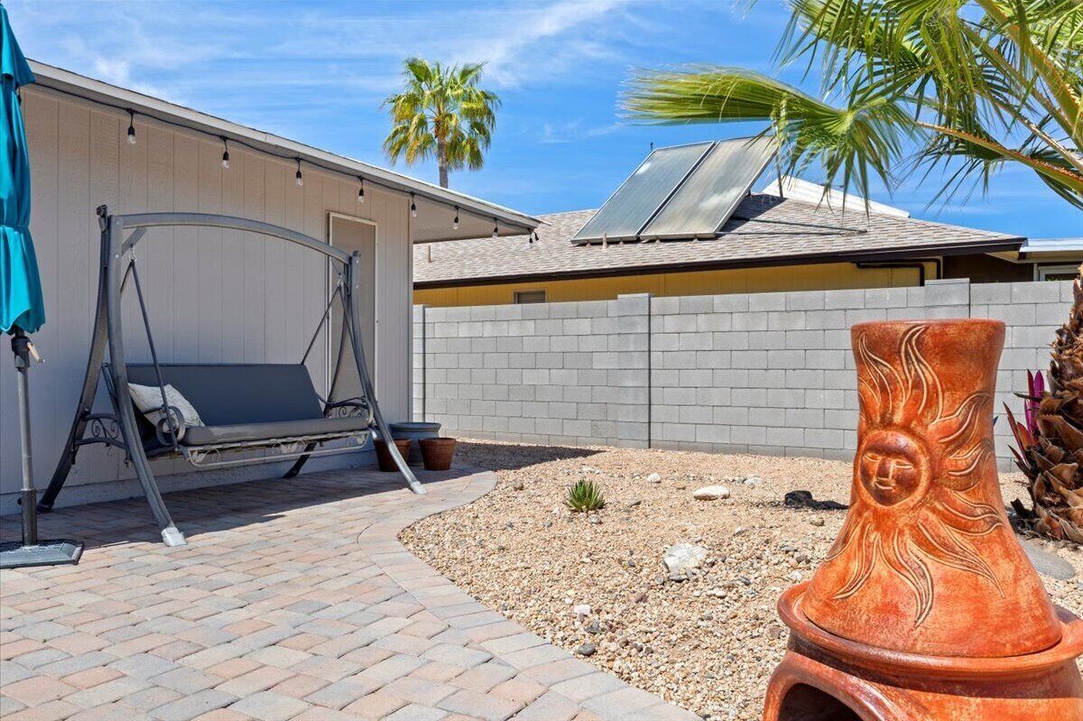 A patio with a swing, a solar panel, a decorative pot, and a palm tree.