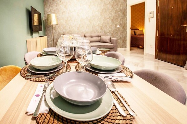 A dining table set with plates, glasses, and cutlery, with a sofa and a lamp in the background.