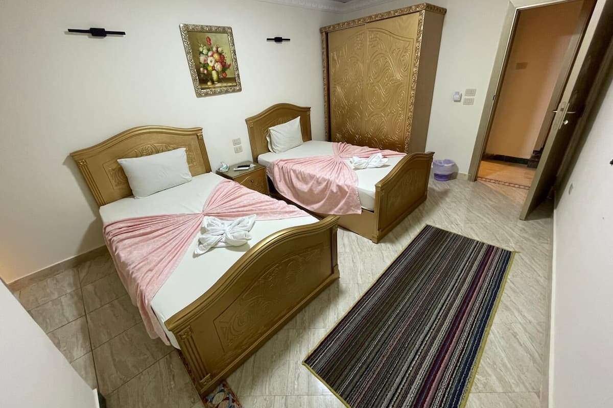 A hotel room with two beds, a large wardrobe, a striped rug, and a painting on the wall.