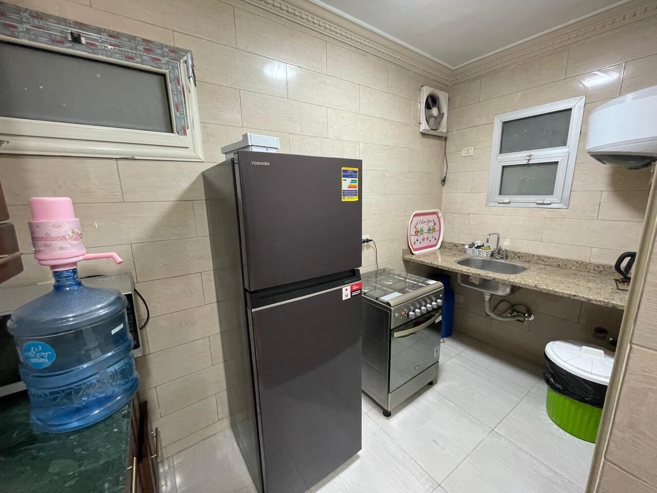 Een kleine keuken met een koelkast, fornuis, spoelbak en een waterdispenser.