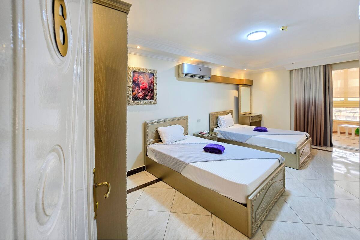 A hotel room with two beds, a large mirror, an air conditioning unit, and a balcony with a view.