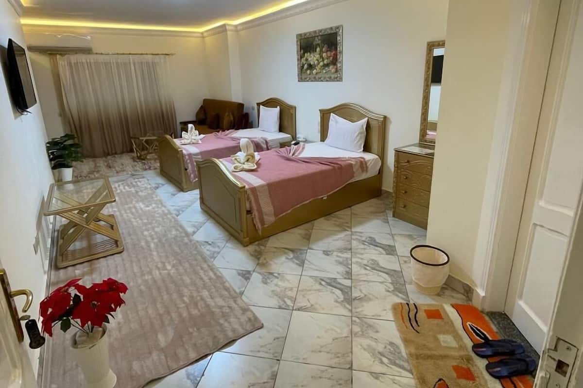 A hotel room with two beds, a sitting area, a TV, a painting, and a bathroom.